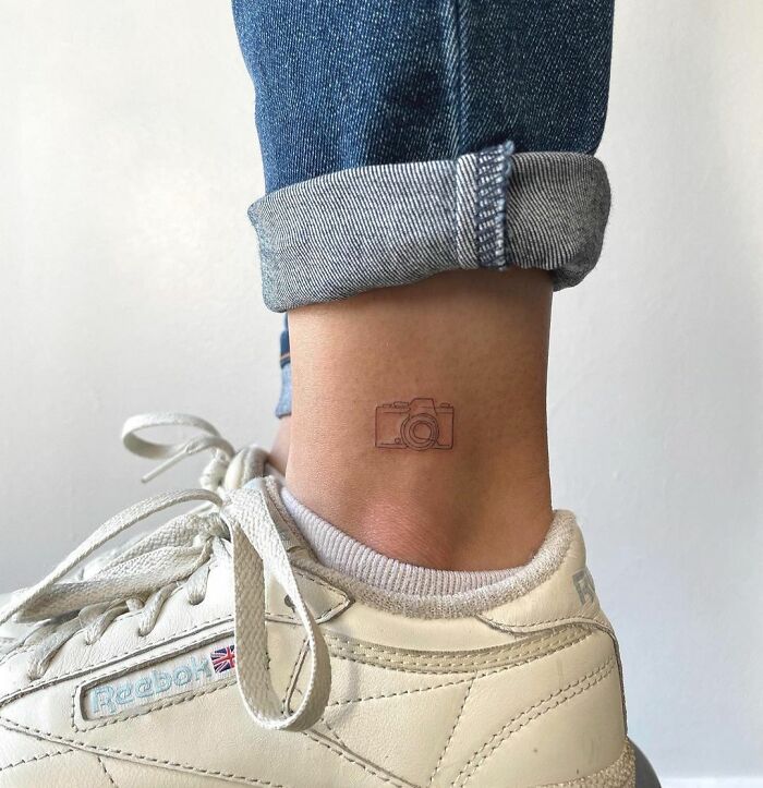 Ankle tattoo of a camera with rolled jeans and white sneakers, exemplifying tattoo care and inspiration.