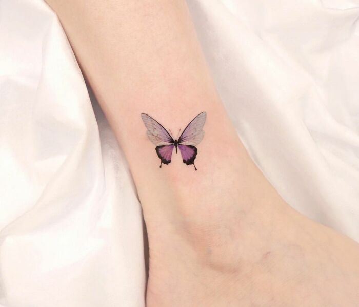 Butterfly ankle tattoo on light skin, showcasing delicate black and purple wings for tattoo inspiration.