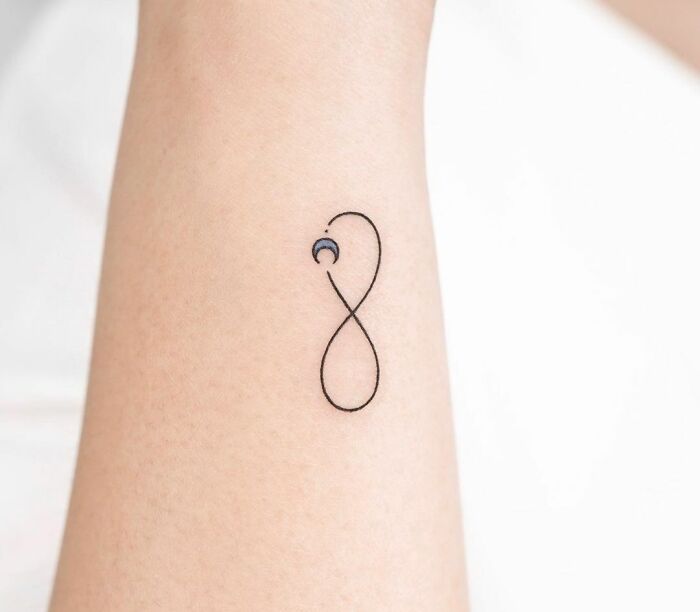 Minimalist infinity tattoo with a crescent moon, symbolizing eternal creativity on forearm.