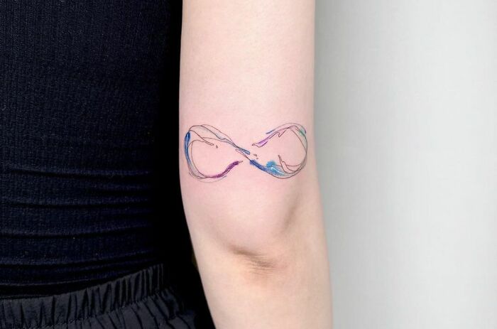 Minimalist infinity tattoo with colorful accents displayed on a person's arm, symbolizing eternal creativity.