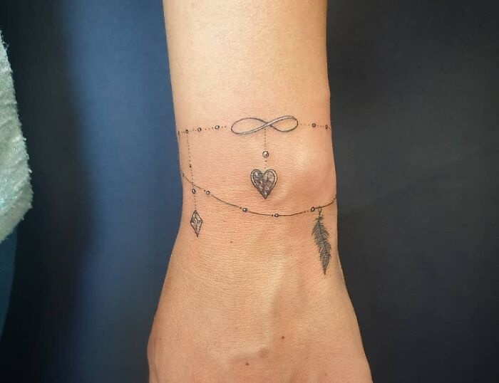Infinity tattoo with heart and feather designs on wrist, showcasing creative eternal themes.