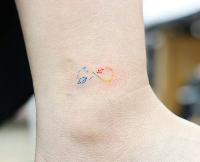 Colorful infinity tattoo on wrist with stars and planets symbolizing eternal creativity.