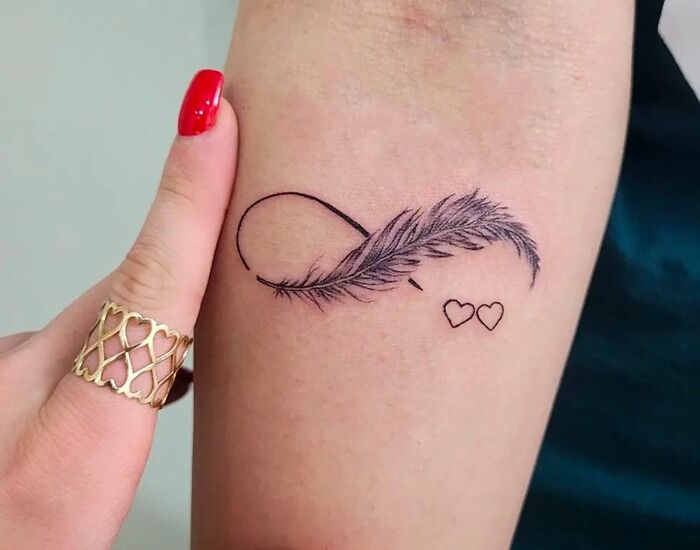 Infinity tattoo with a feather and hearts, showcasing eternal creativity on a person's arm.