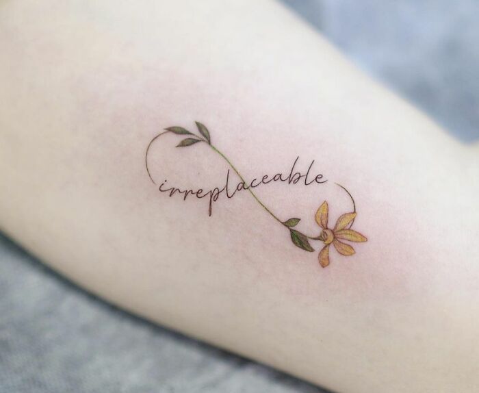 Infinity tattoo with "irreplaceable" script intertwined with a delicate flower design.