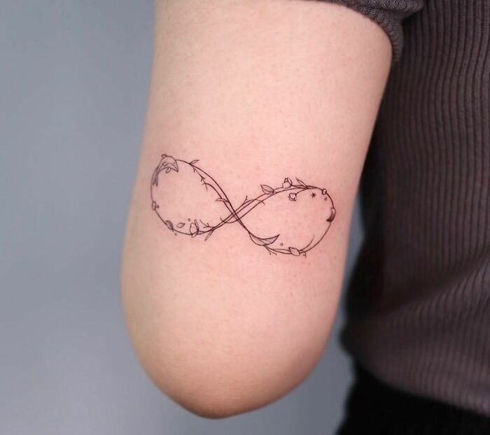 Infinity tattoo with delicate floral design on an arm, showcasing eternal creativity.