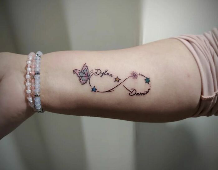 Infinity tattoo featuring butterfly and stars on forearm, symbolizing creativity.