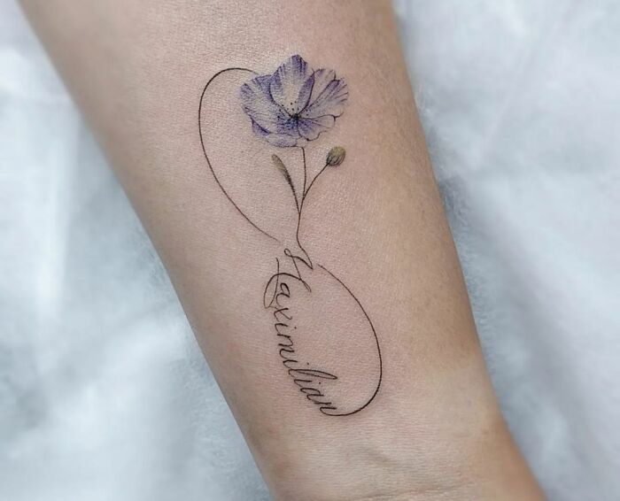 Infinity tattoo with a flower and the name Maximilian, symbolizing eternal creativity on a person's forearm.