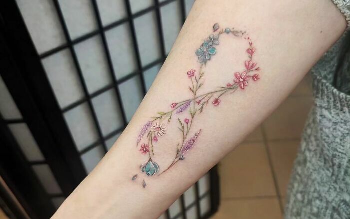 Floral infinity tattoo on forearm, showcasing creativity and eternity with delicate pink and blue flowers.