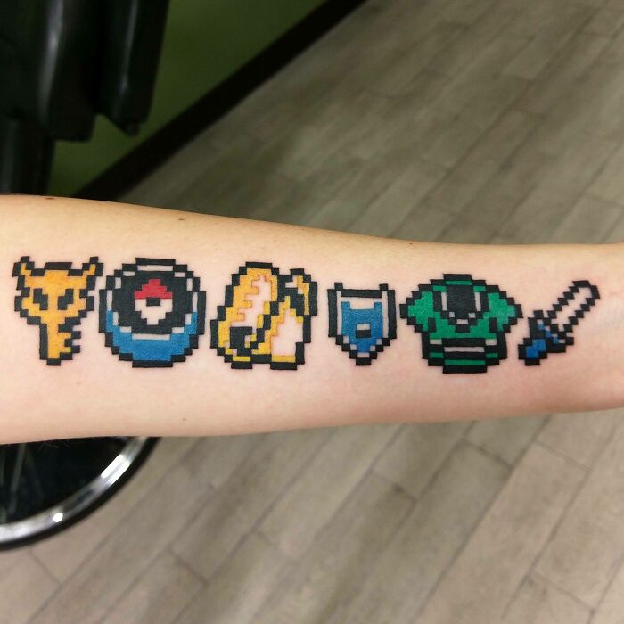 Pixelated The Legend Of Zelda video game tattoos on an arm, featuring various iconic symbols for hardcore gamers.