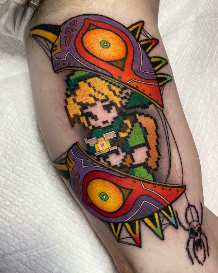The Legend Of Zelda video game tattoo featuring a pixel art character with a colorful mask design on an arm.