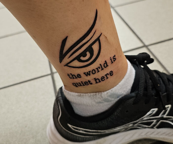 Ankle tattoo featuring an eye design and "the world is quiet here" text above a black sneaker.