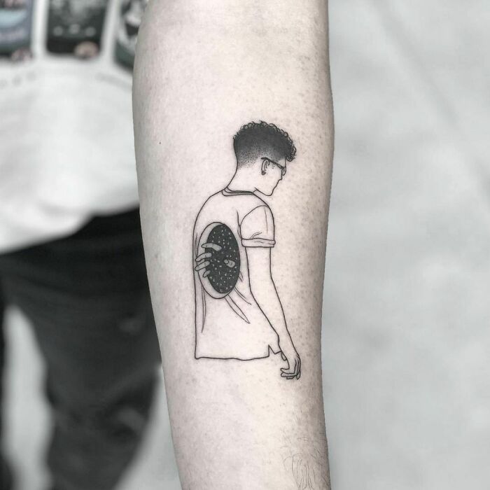 Tattoo of a person in profile with a hand holding a planet behind their back, symbolizing mental health and healing.