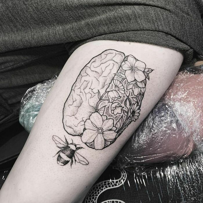 Tattoo of a brain with flowers and a bee, symbolizing mental health and healing, on a person's arm.