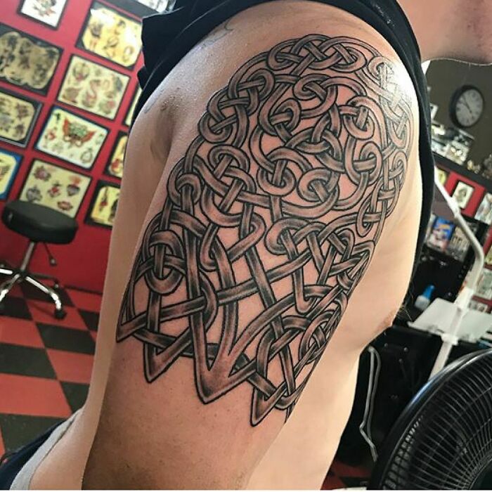 Detailed tribal tattoo on a person's arm, featuring intricate knotwork in a tattoo parlor setting.