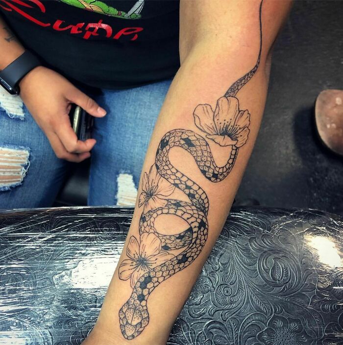 Forearm tattoo of a snake intertwined with flowers, showcasing intricate snake tattoo design.
