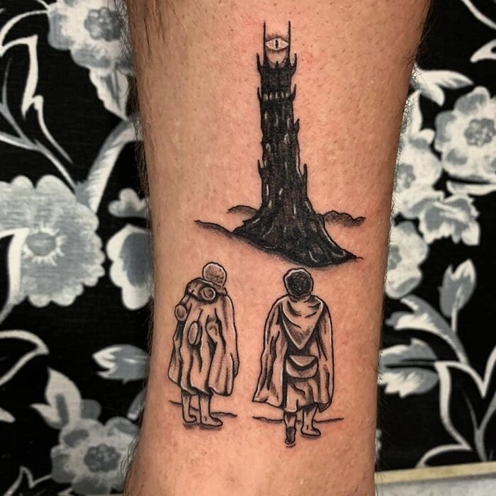 "Lord of the Rings tattoo featuring two cloaked figures facing a dark tower with an eye on top, floral background."