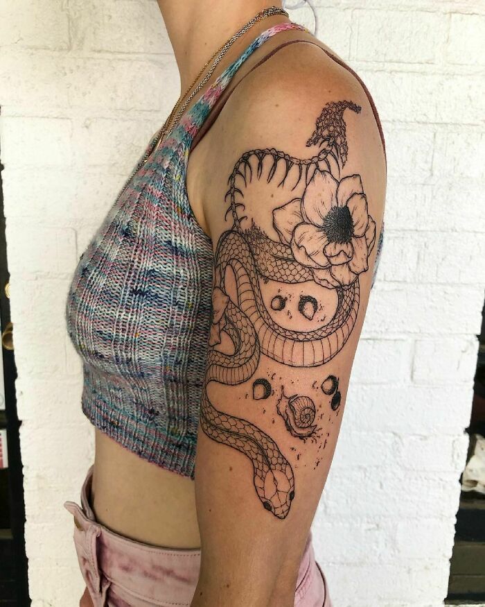 Person with a detailed snake tattoo on their upper arm, featuring flowers and abstract elements.