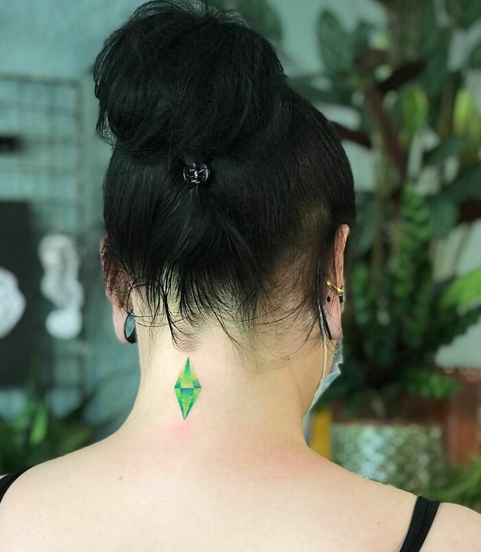 The Sims video game tattoo showcasing a vivid green diamond shape on the back of the neck, inspired by a video game design.