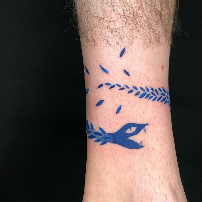 Blue snake tattoo design wrapped around a wrist, featuring sharp fangs and minimalist leaf accents.