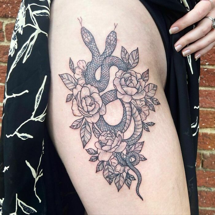 Intricate snake tattoo intertwined with flowers on upper arm, emphasizing snake tattoos.