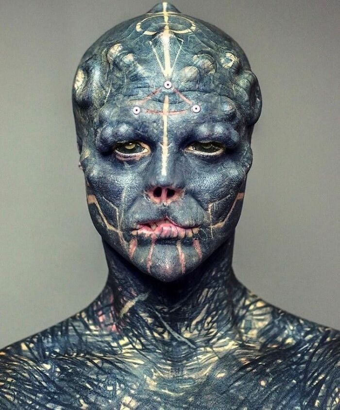 Person with extensive body modifications resembling an alien, showcasing detailed tattoos and unique features. Person with extensive body modifications resembling an alien, showcasing detailed tattoos and unique features.