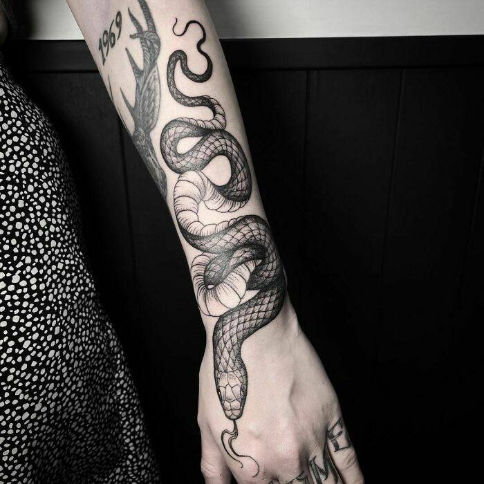 Black snake tattoo winding down a person's forearm.