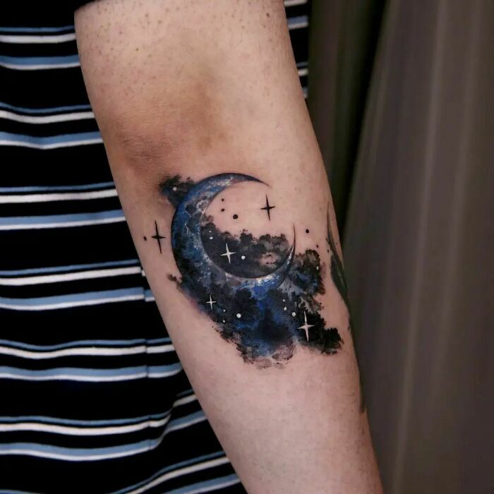 Moon and stars design on an elbow tattoo in cosmic style.