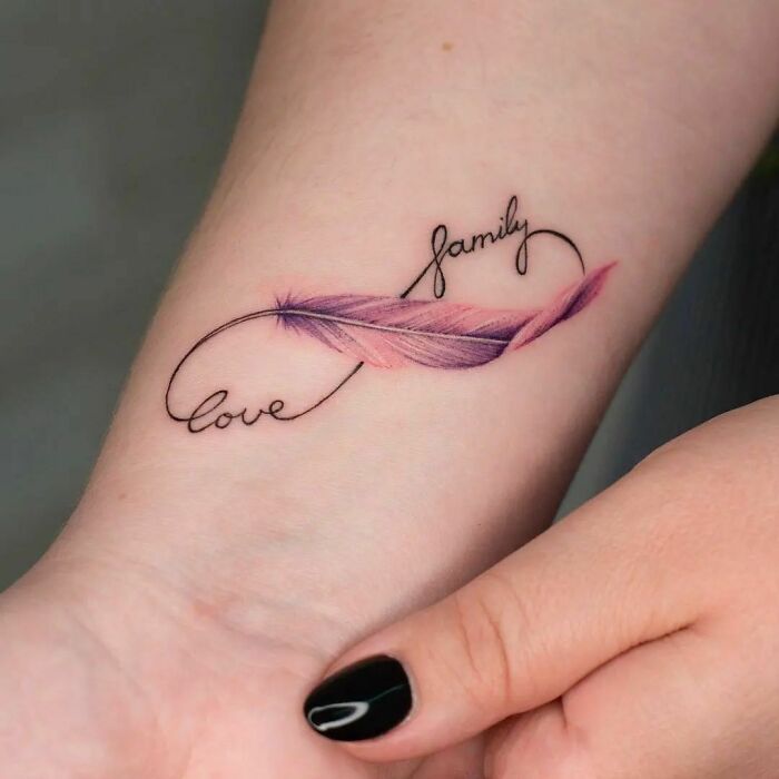 Infinity tattoo with a feather design and the words "love" and "family" on a wrist, showcasing eternal creativity.