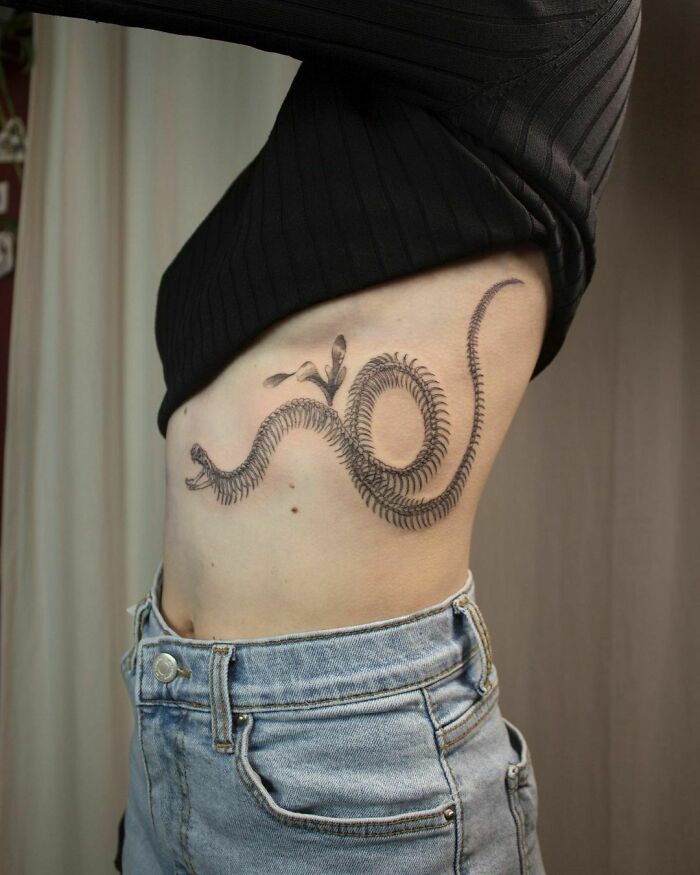 Side view of a person with a detailed snake tattoo curving along their ribs.
