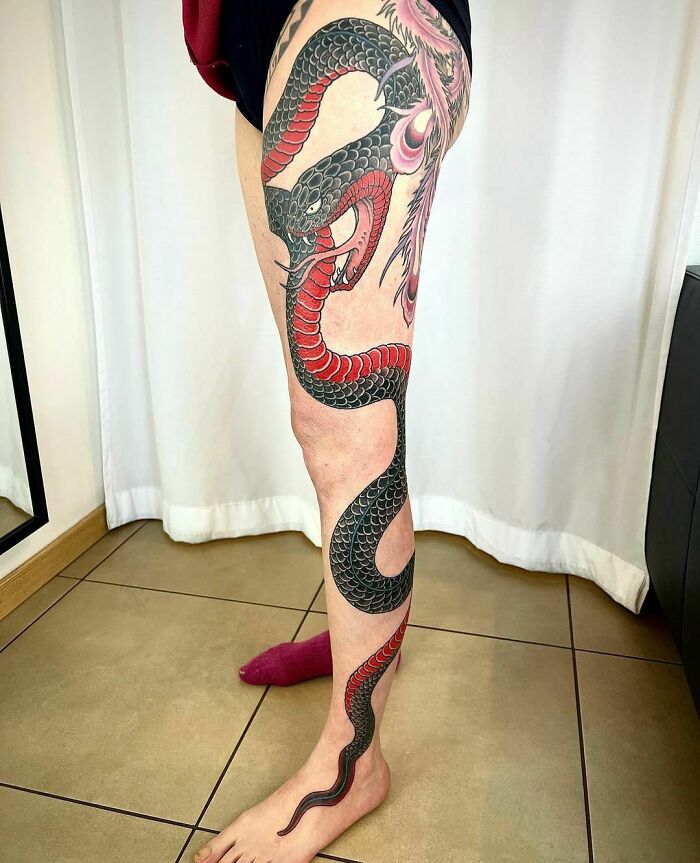 Snake tattoo design wrapped around a person's leg, featuring intricate black and red details.