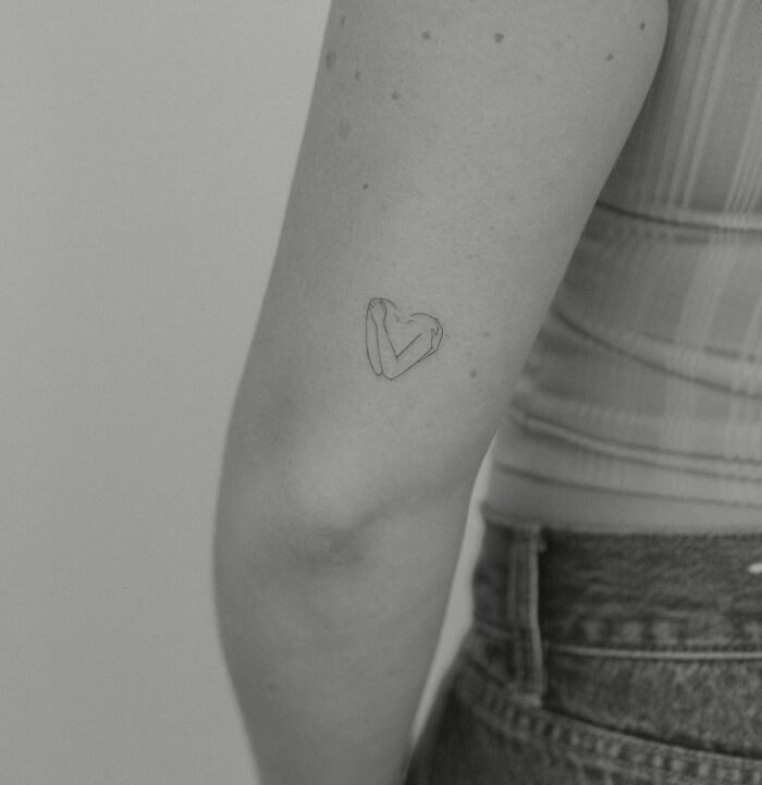 Minimalist heart elbow tattoo design on person's arm wearing a striped top.