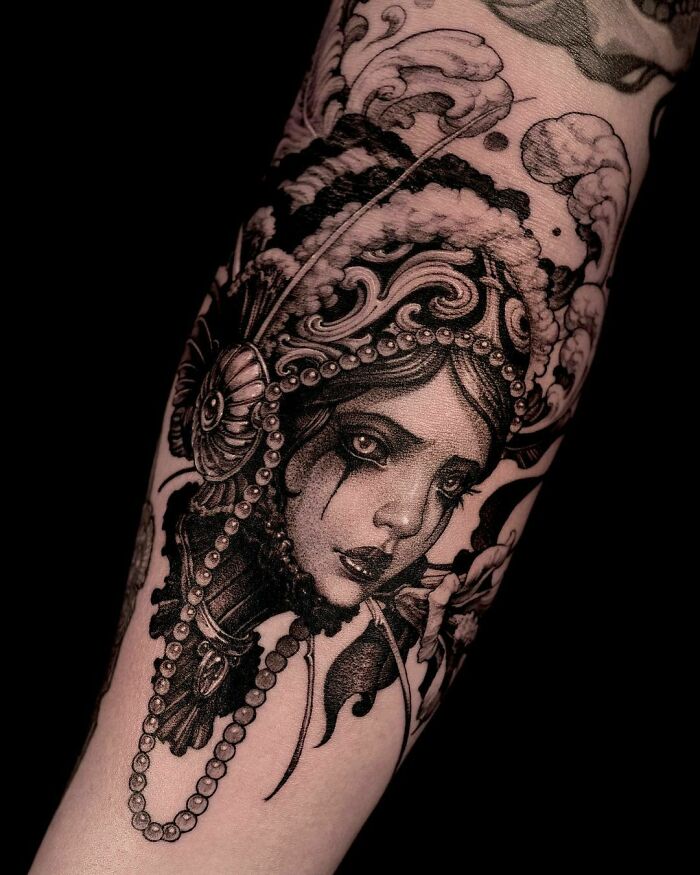 Gothic tattoo of an ornate woman's face, detailed with pearls and intricate patterns on an arm.