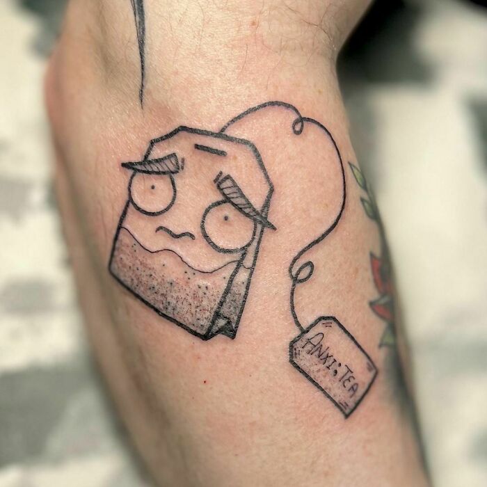 Tattoo of a teabag with a worried face, labeled "Anxie-tea," symbolizing mental health healing.