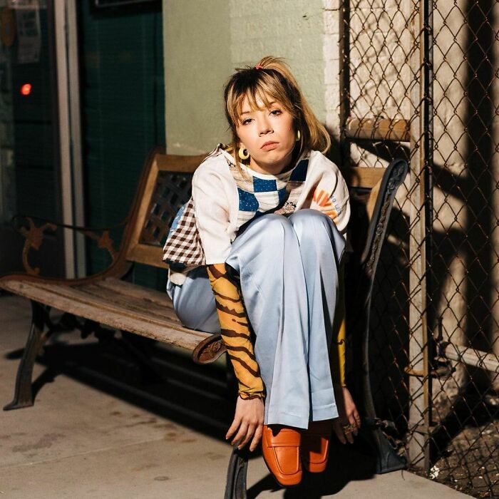 A young woman with a contemplative expression sits on a bench, wearing a stylish outfit. A young woman with a contemplative expression sits on a bench, wearing a stylish outfit.