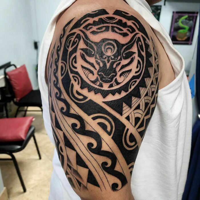 A detailed tribal tattoo featuring intricate animal and geometric patterns on an upper arm.