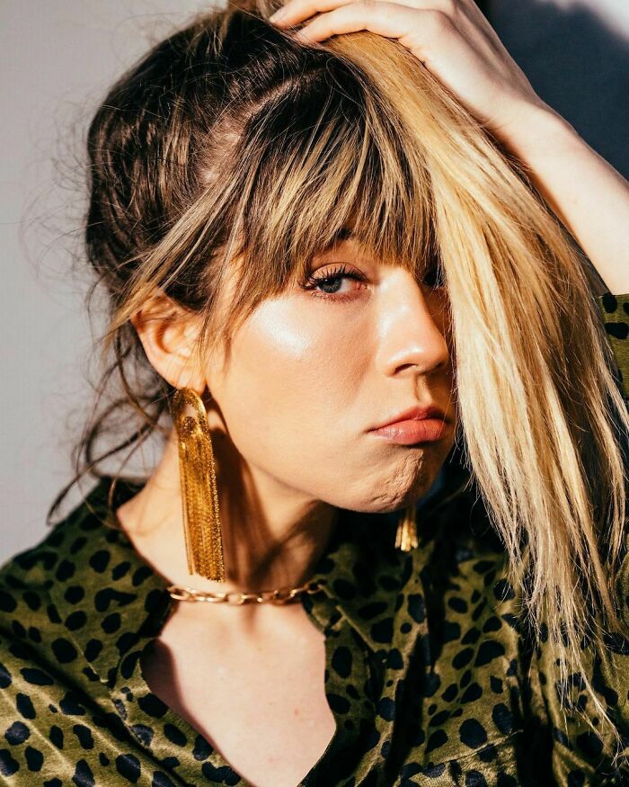 Young woman with blonde hair and long earrings, wearing a green patterned blouse, posing thoughtfully. Young woman with blonde hair and long earrings, wearing a green patterned blouse, posing thoughtfully.