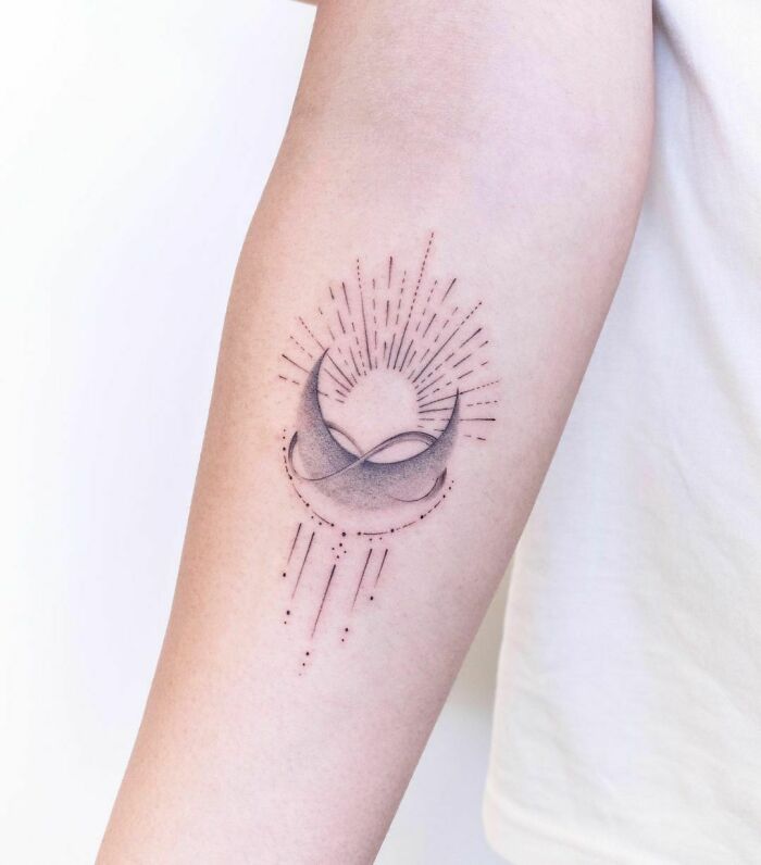 Infinity tattoo with crescent moon and sunburst lines on forearm.