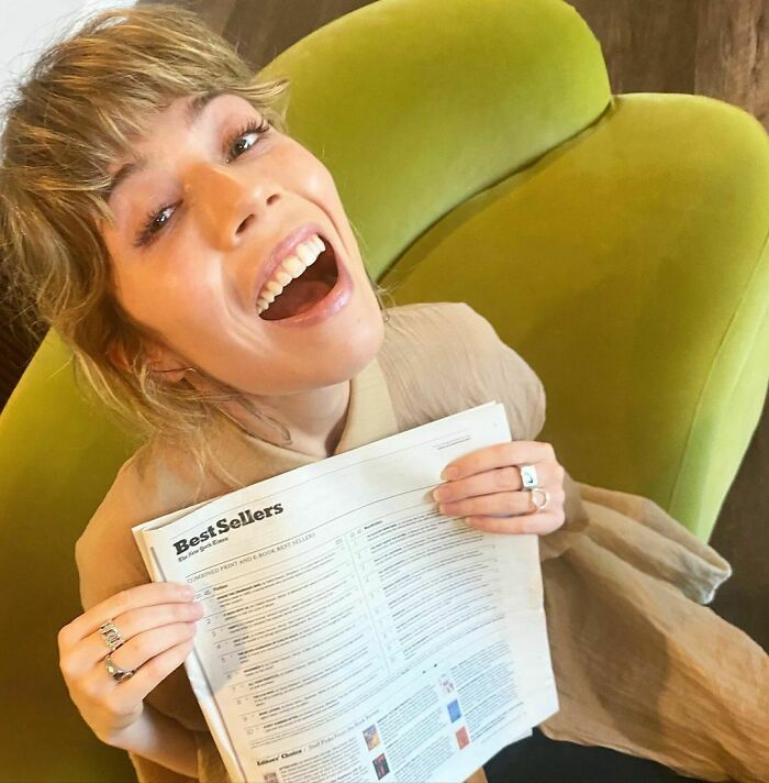 Smiling woman holding a best sellers list, sitting on a green couch. Smiling woman holding a best sellers list, sitting on a green couch.