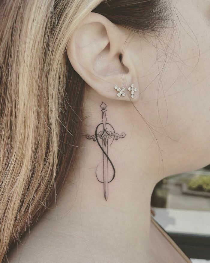Infinity tattoo behind the ear, featuring a sword intertwined with elegant loops.