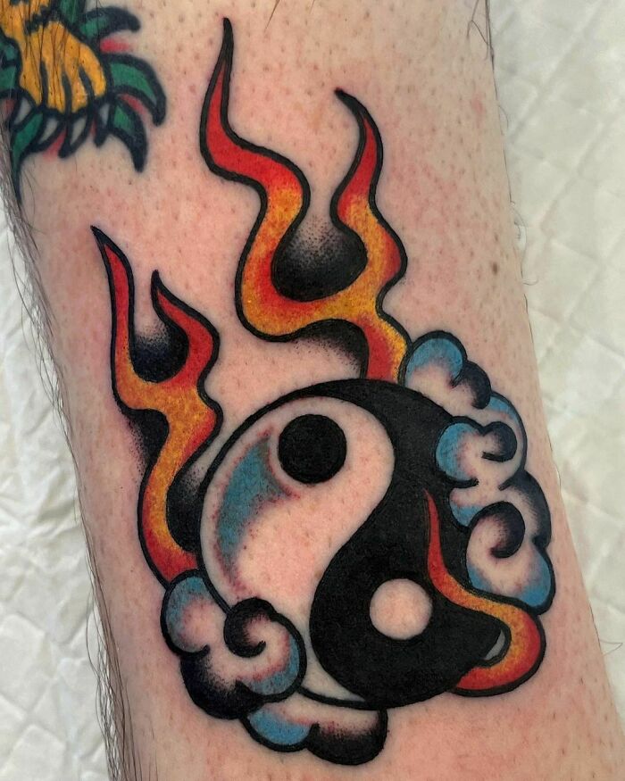 Yin Yang tattoo with flames and clouds, symbolizing duality.