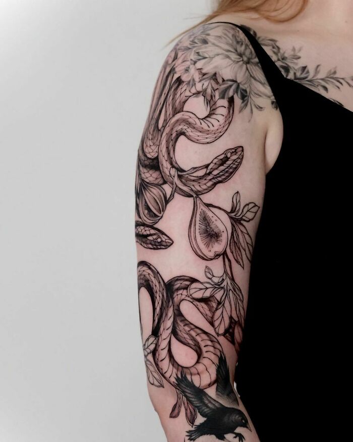 Arm with detailed snake tattoo design featuring fig elements and leaves.