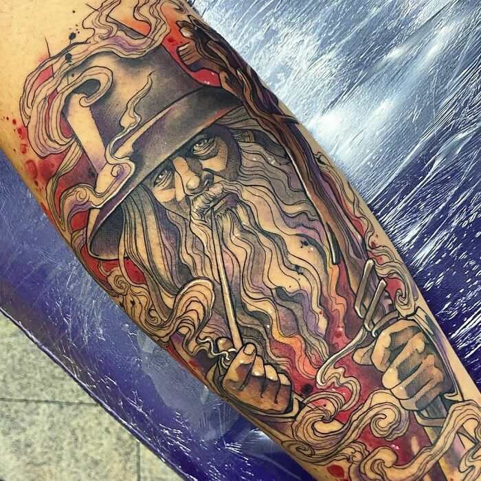 Tattoo of a wizard with long hair and beard, wearing a hat, from Lord of the Rings, with vibrant colors and swirling designs.
