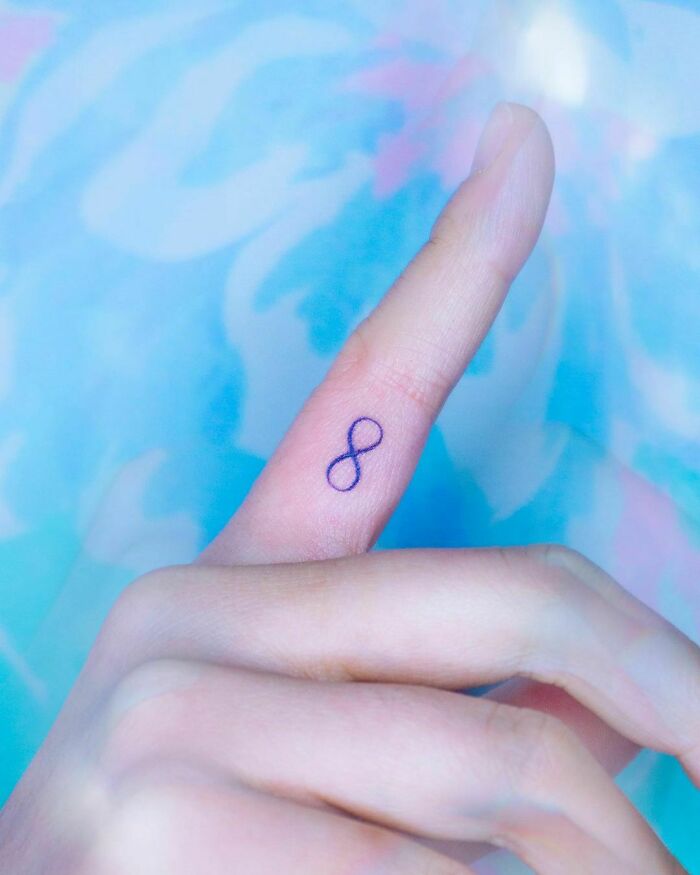 Infinity tattoo on a finger, showcasing eternal creativity against a colorful background.
