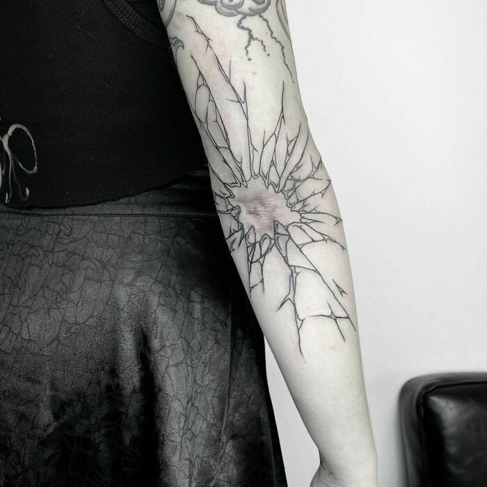 Geometric elbow tattoo with c*****d design on a woman's arm, wearing a black shirt.
