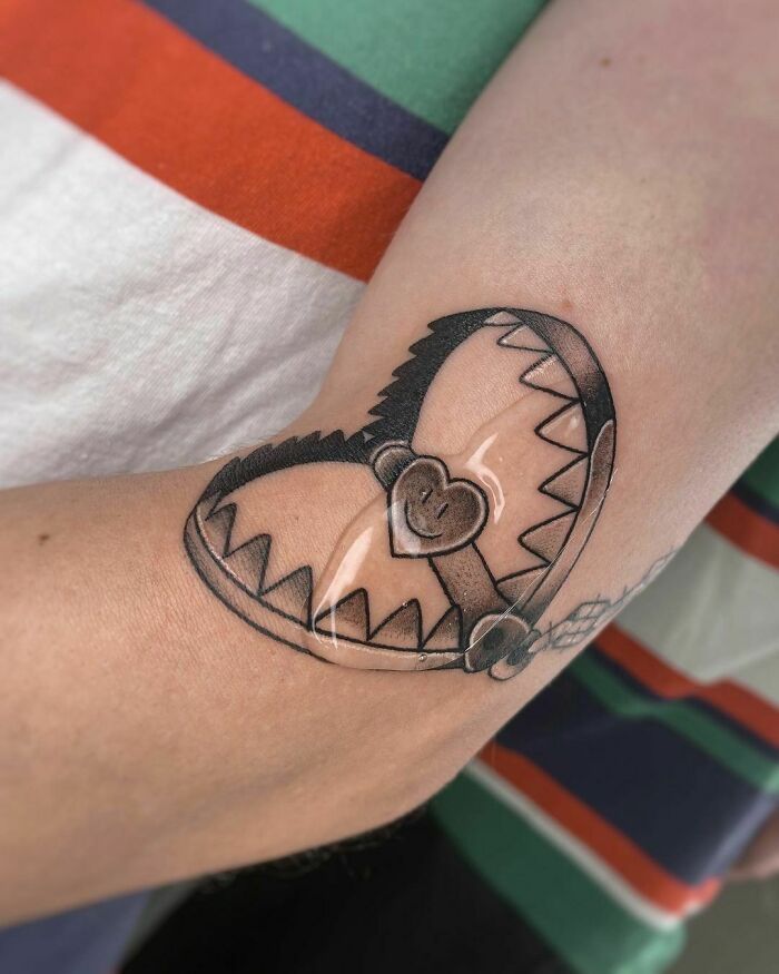 Elbow tattoo featuring a heart-shaped bear trap design on an arm wearing a striped shirt.