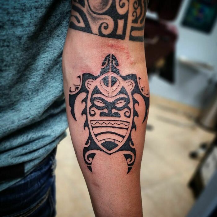 Arm with detailed tribal tattoo featuring bold black tribal patterns.