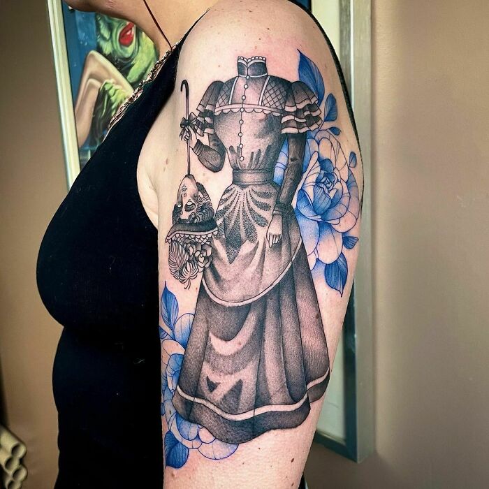 Gothic tattoo of a headless woman in Victorian dress on arm, adorned with blue floral patterns.