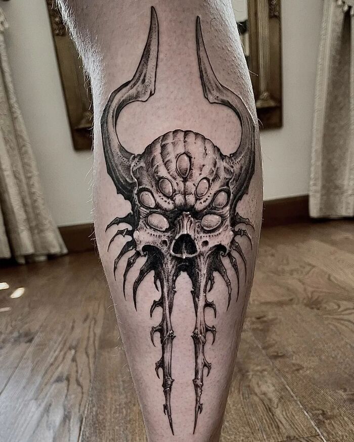 Intricate gothic tattoo design featuring a horned skull with symmetrical patterns on a person's calf.