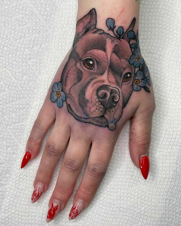 Dog-themed memorial tattoo on hand with blue flowers, honoring family.