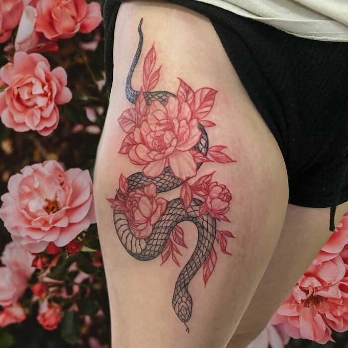 Snake tattoo intertwined with pink flowers on a thigh, capturing artistic design and intricate details.